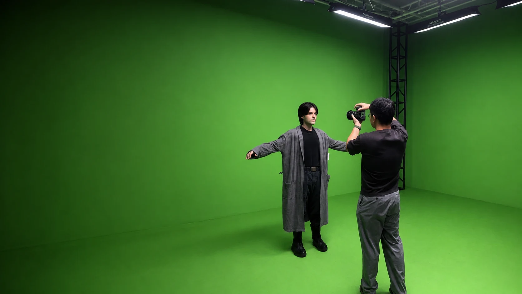 A camera operator films a performer on a green-screen production stage.